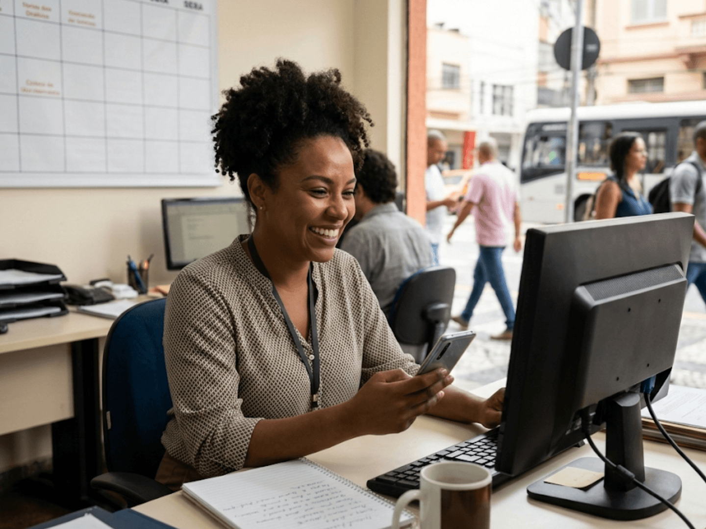 Empreendedora conferindo mensagens no celular com sistema de gestão no computador ao lado